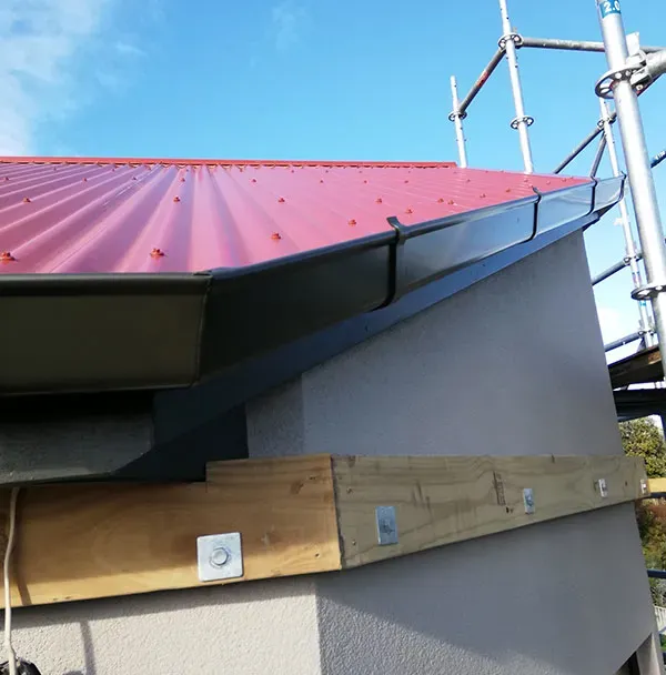 New dark colour steel spouting fitted along a bevelled rake over a red roof